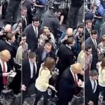 In new footage, the reporter (in cream jacket) is seen alongside Mr Trump before being held back