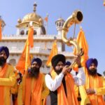 An Indian Sikh devotee plays a musical instrument as he walks with Punj Pyara holding flags