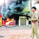 This photo, taken on March 1, 2002, shows a policeman as he walks in front of a row of burning shops in Ahmedabad.