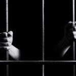 Conceptual monochrome photo of hands holding the bars of a prison door