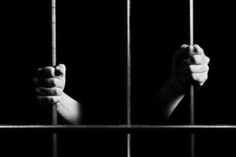 Conceptual monochrome photo of hands holding the bars of a prison door